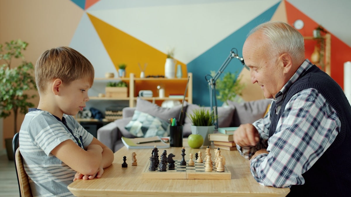 Portrait of grandfather and grandson playing chess moving chessmen on board enjoying game at home. Intellectual hobby, people and happy family concept.